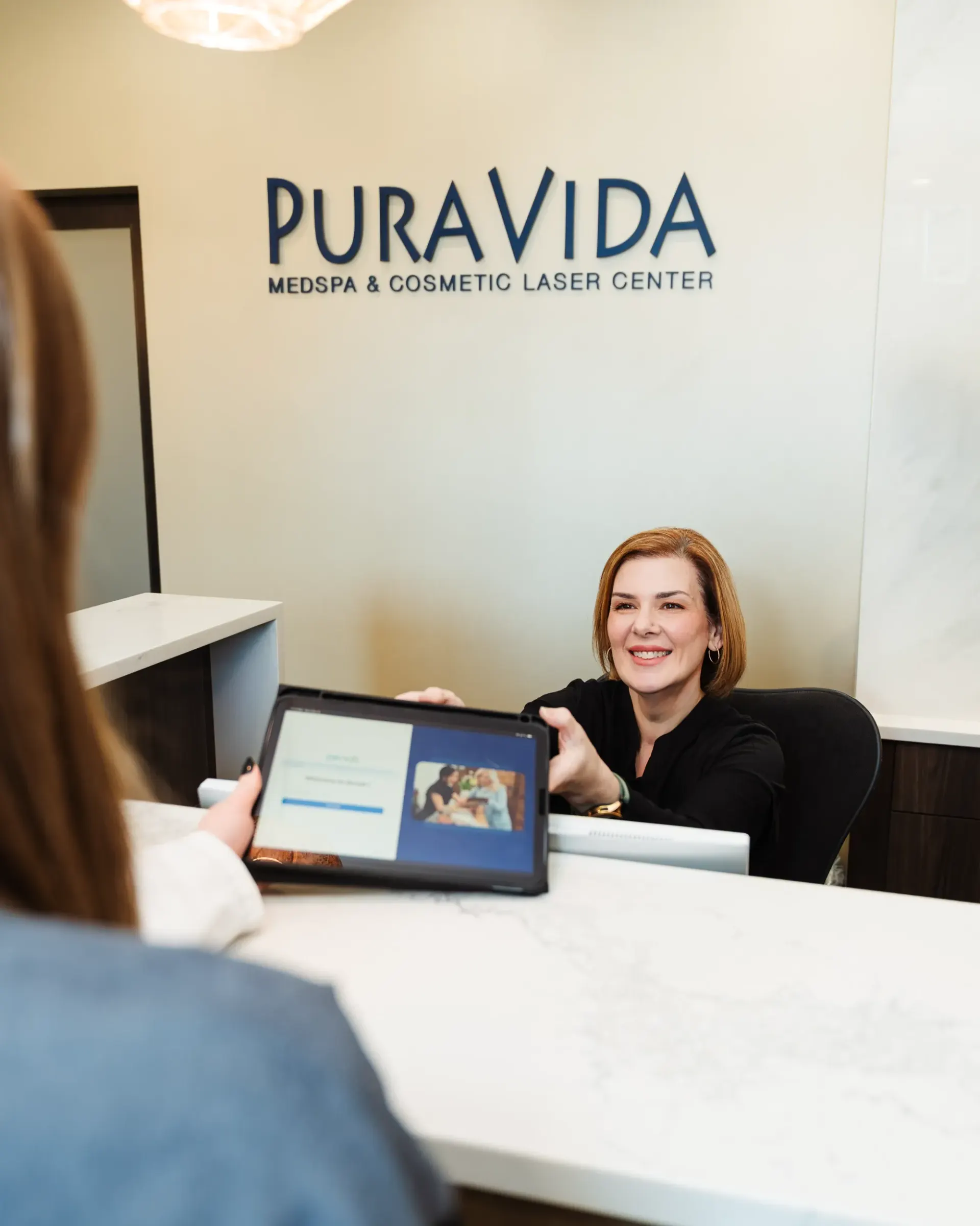 Staff member showing a tablet to a client at the Pura Vida front desk