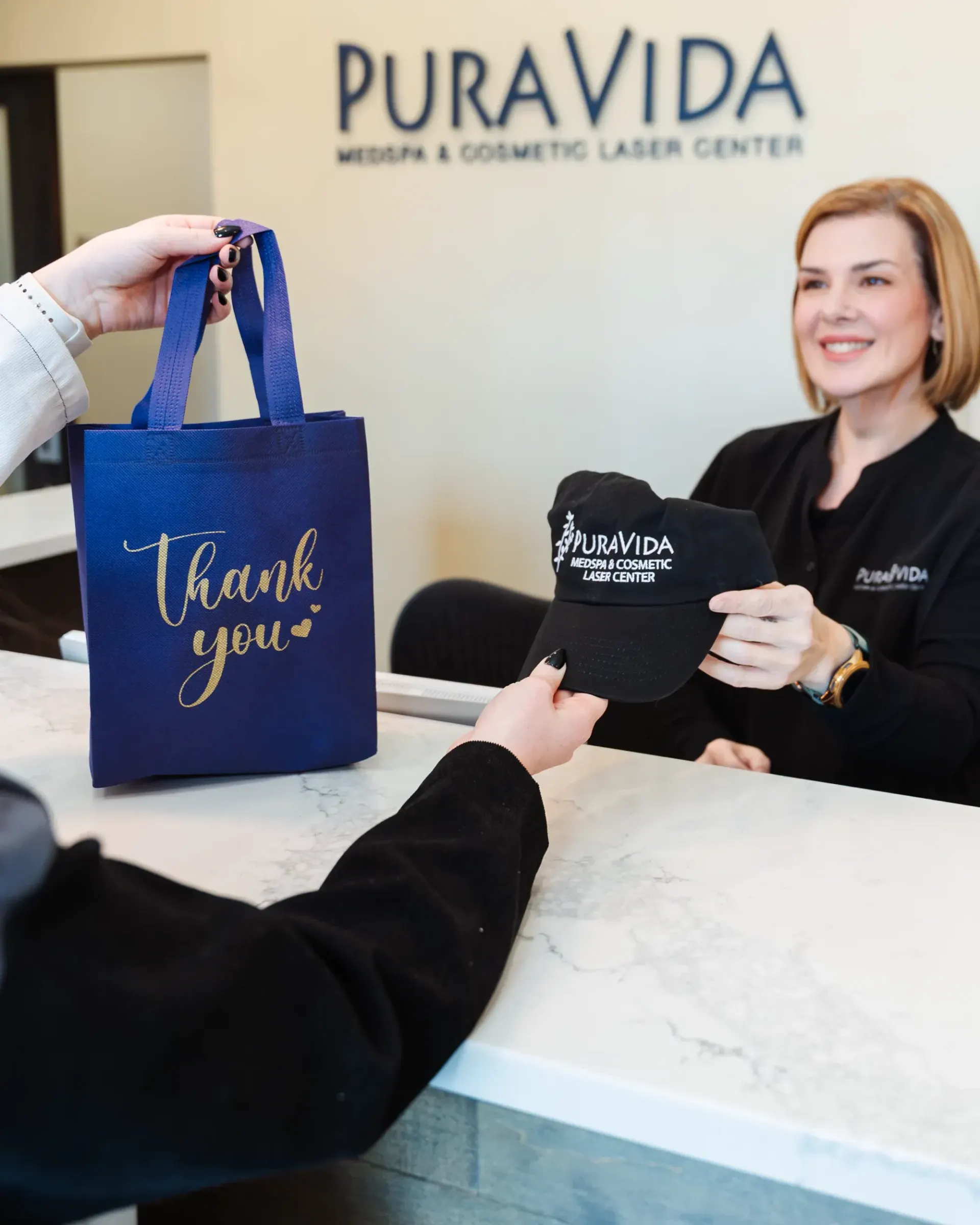 Pura Vida receptionist handing a thank-you gift bag to a client at reception