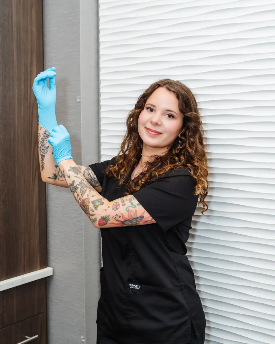 Smiling tattooed staff member in black scrubs holding blue gloves at the clinic