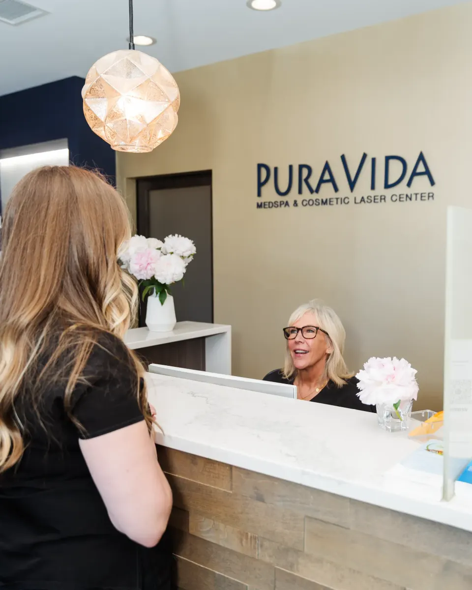 Receptionist smiling at a client across the Pura Vida Med Spa front desk