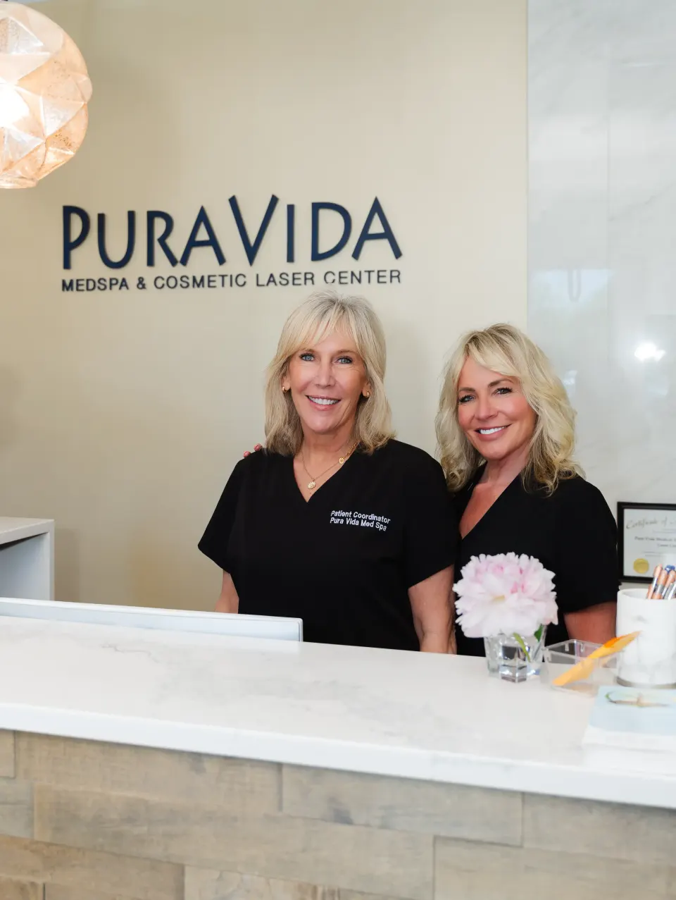 Two smiling staff members standing at the Pura Vida Med Spa reception desk