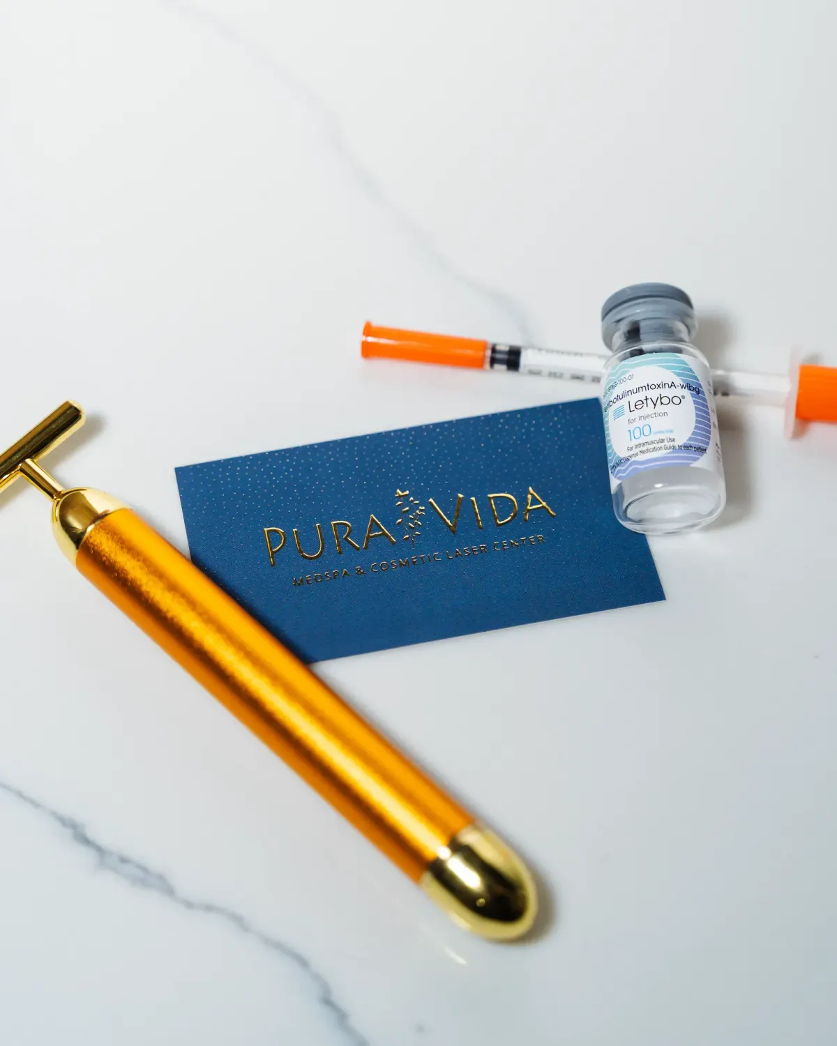 Letybo neurotoxin vial, syringes and gold facial tool on a Pura Vida card
