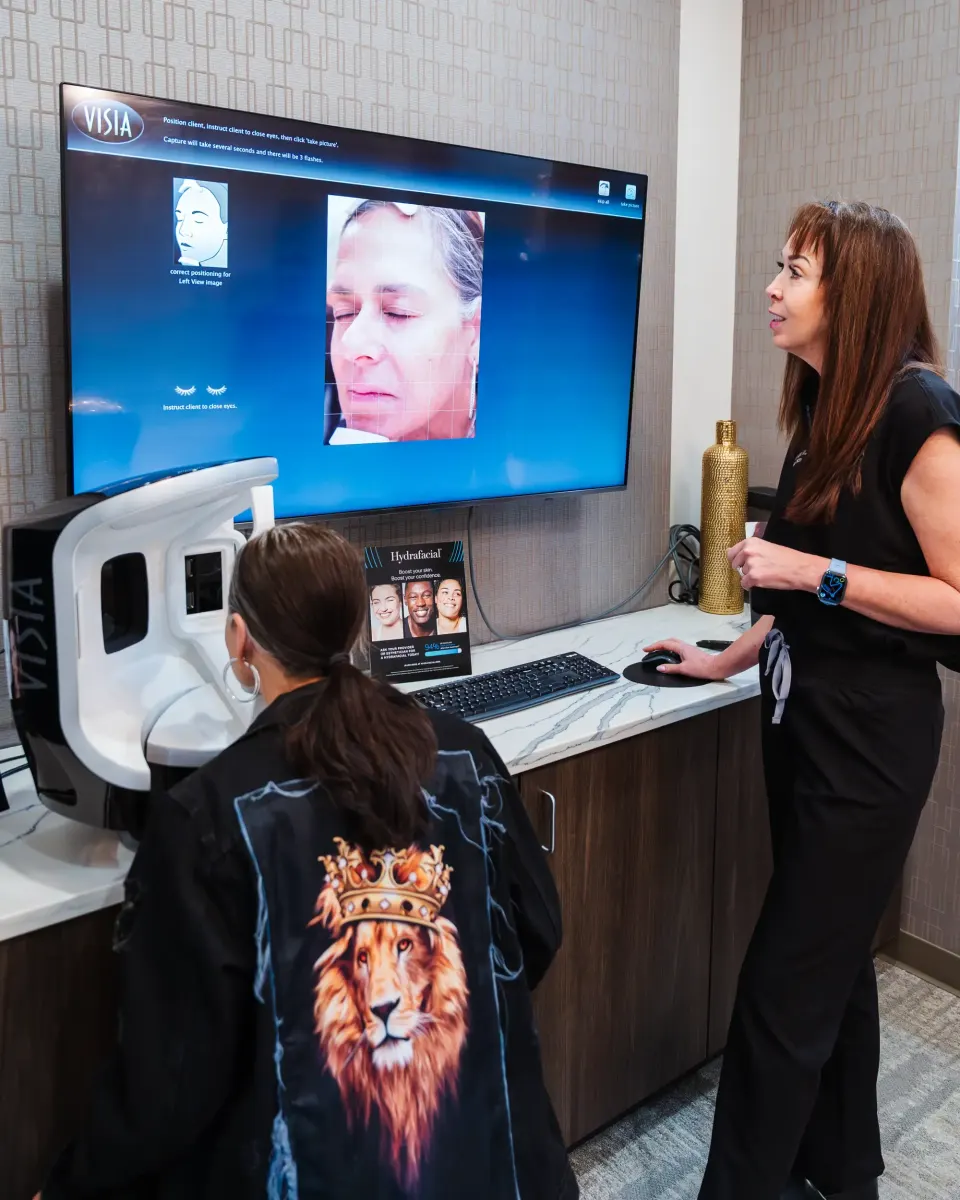 Client seated at a facial skin analysis imaging station with staff assisting