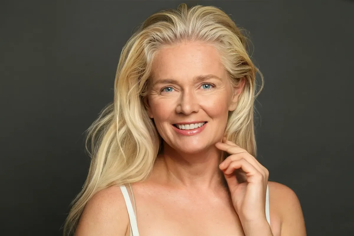 Smiling mature woman with long healthy blonde hair against dark background