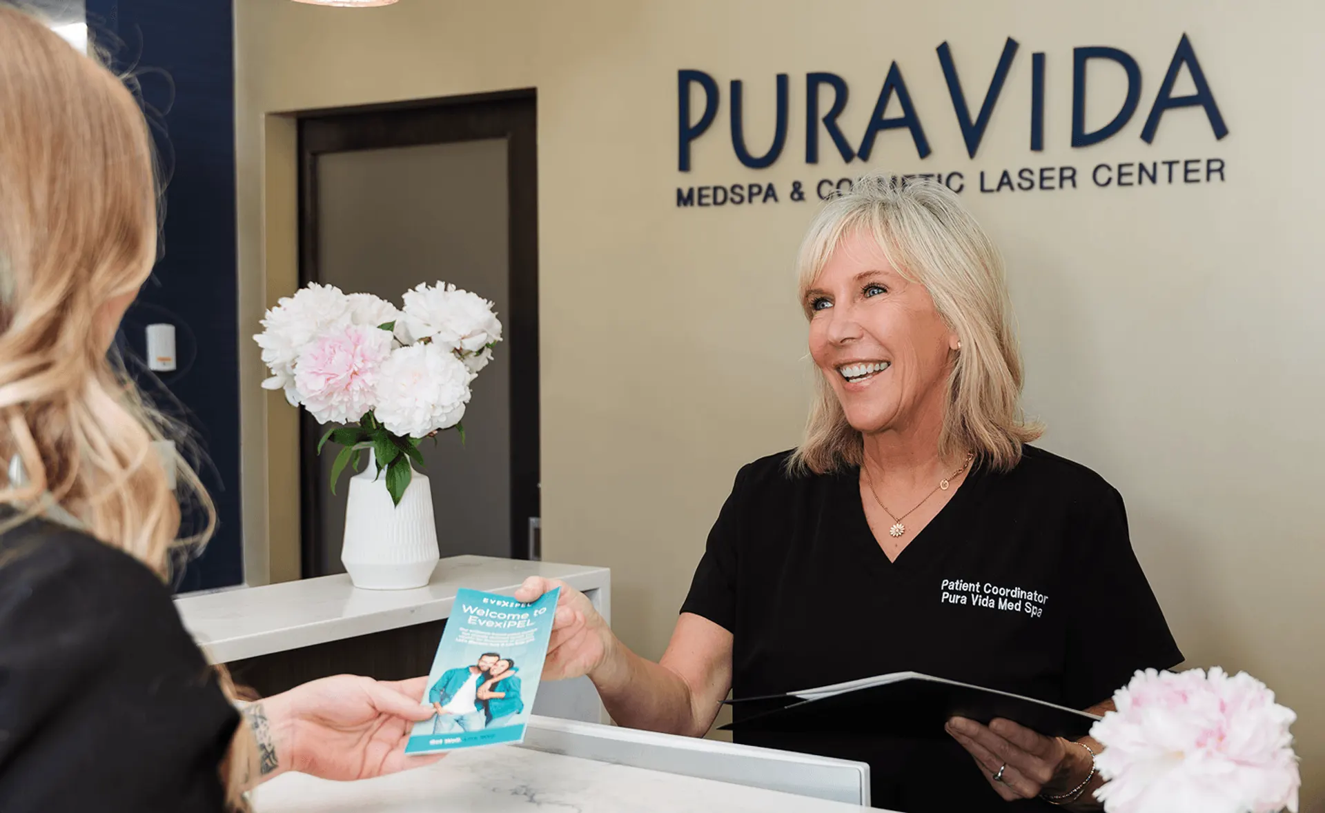 Smiling receptionist handing a brochure to a client at the Pura Vida Med Spa front desk