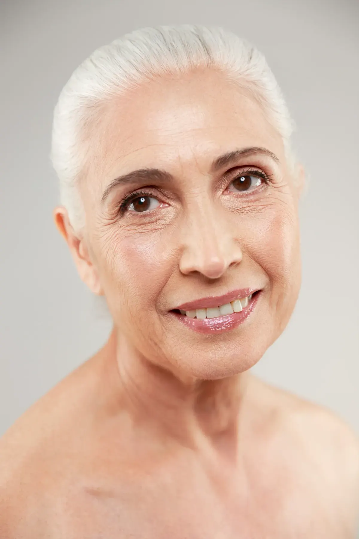 Smiling older woman with silver hair and bare shoulders, natural aging skin