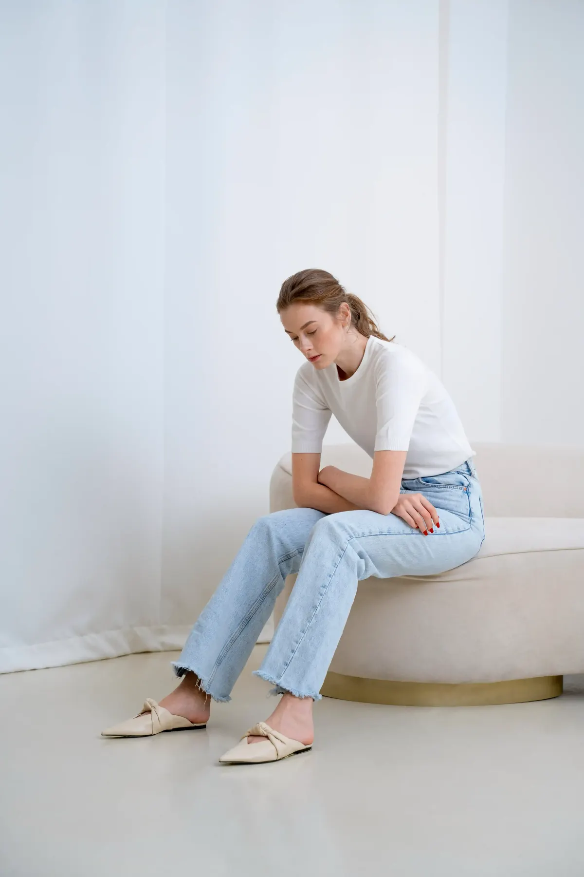 Woman in white top and jeans sitting on bench in bright minimal room