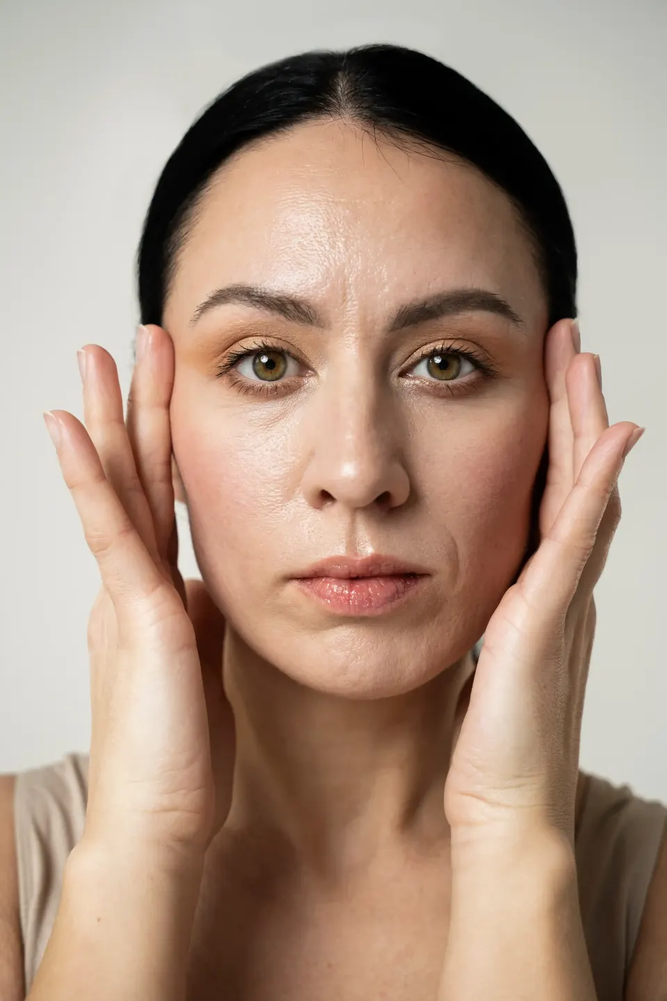 Brunette woman framing her face with both hands, clear complexion