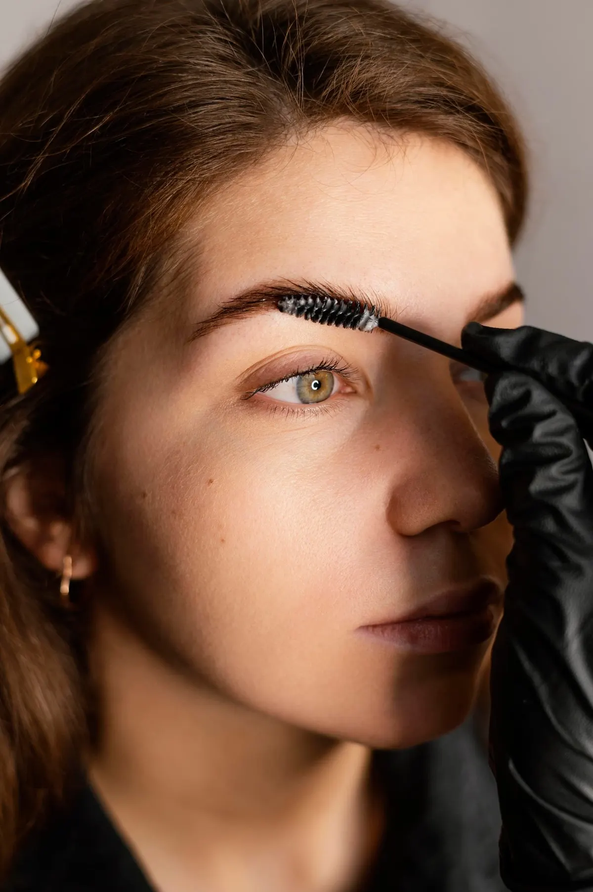 Esthetician brushing a client's eyebrow with a spoolie during grooming