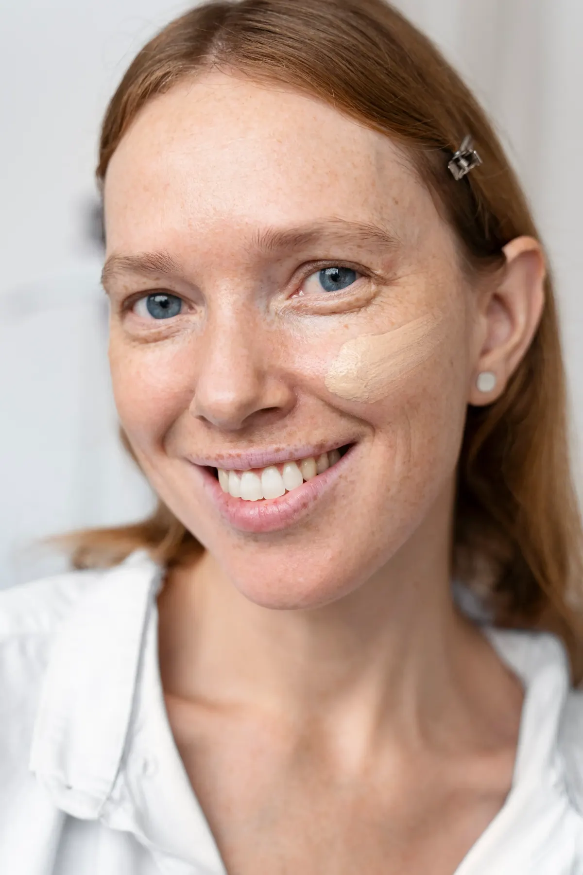 Smiling woman with foundation blended on one cheek showing skin tone difference