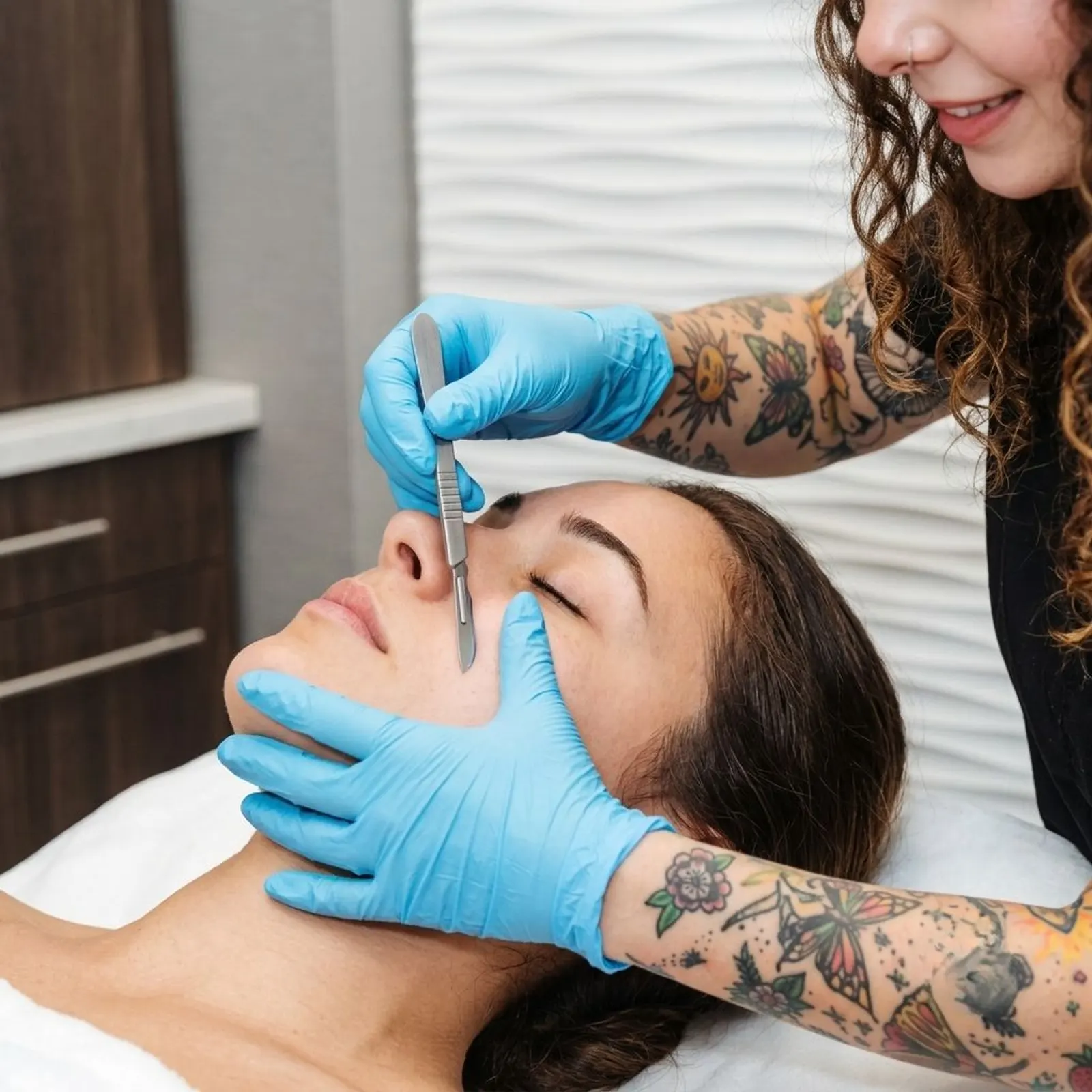 Provider in blue gloves performing a dermaplaning treatment on a woman's face