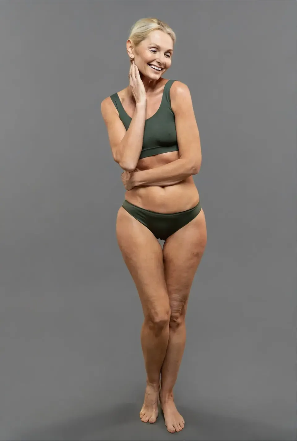 Smiling mature woman in green swimwear posing against a gray backdrop