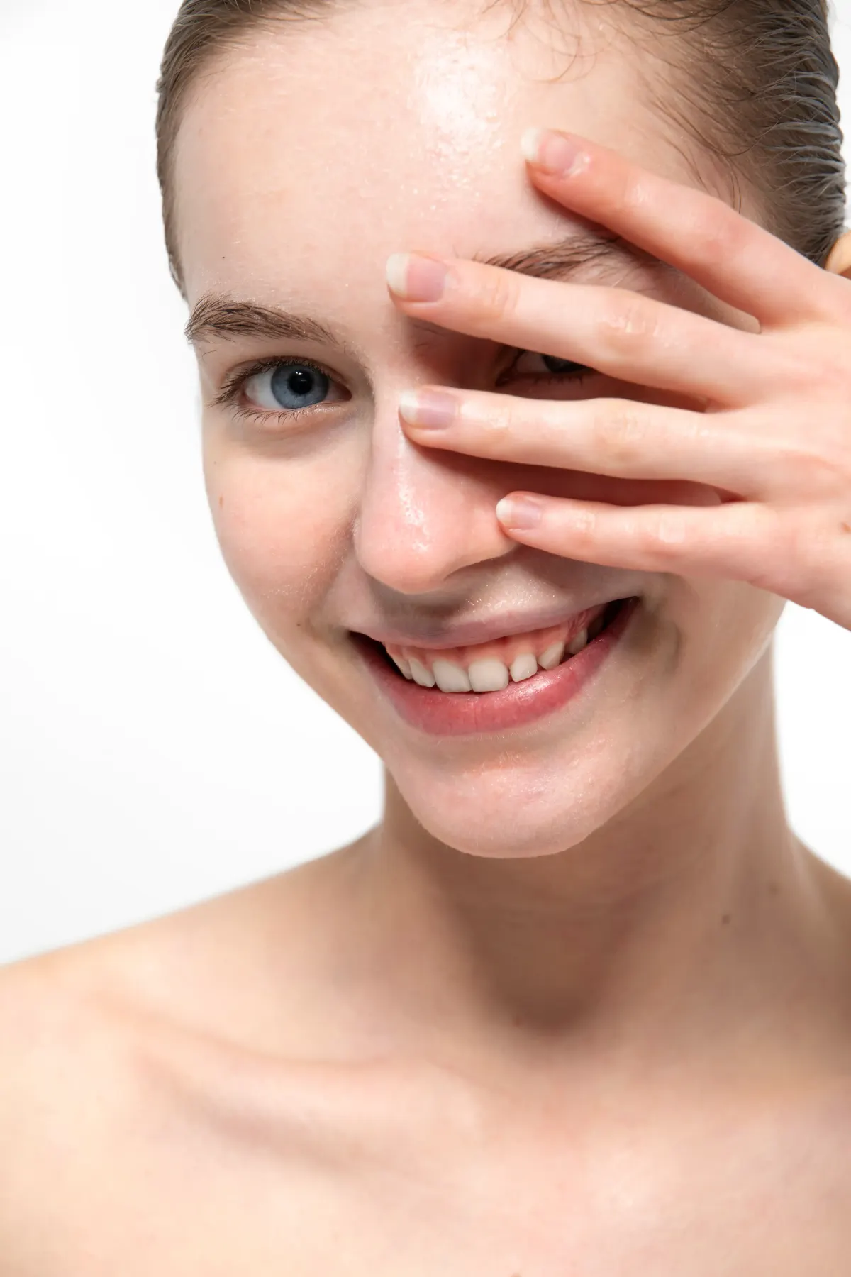 Smiling young woman with clear skin peeking through her fingers