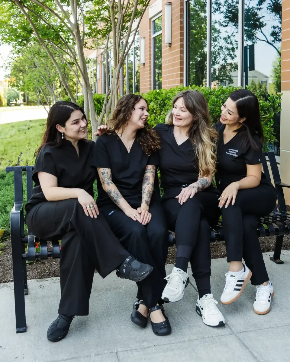 Four Pura Vida staff members in black uniforms chatting on an outdoor bench