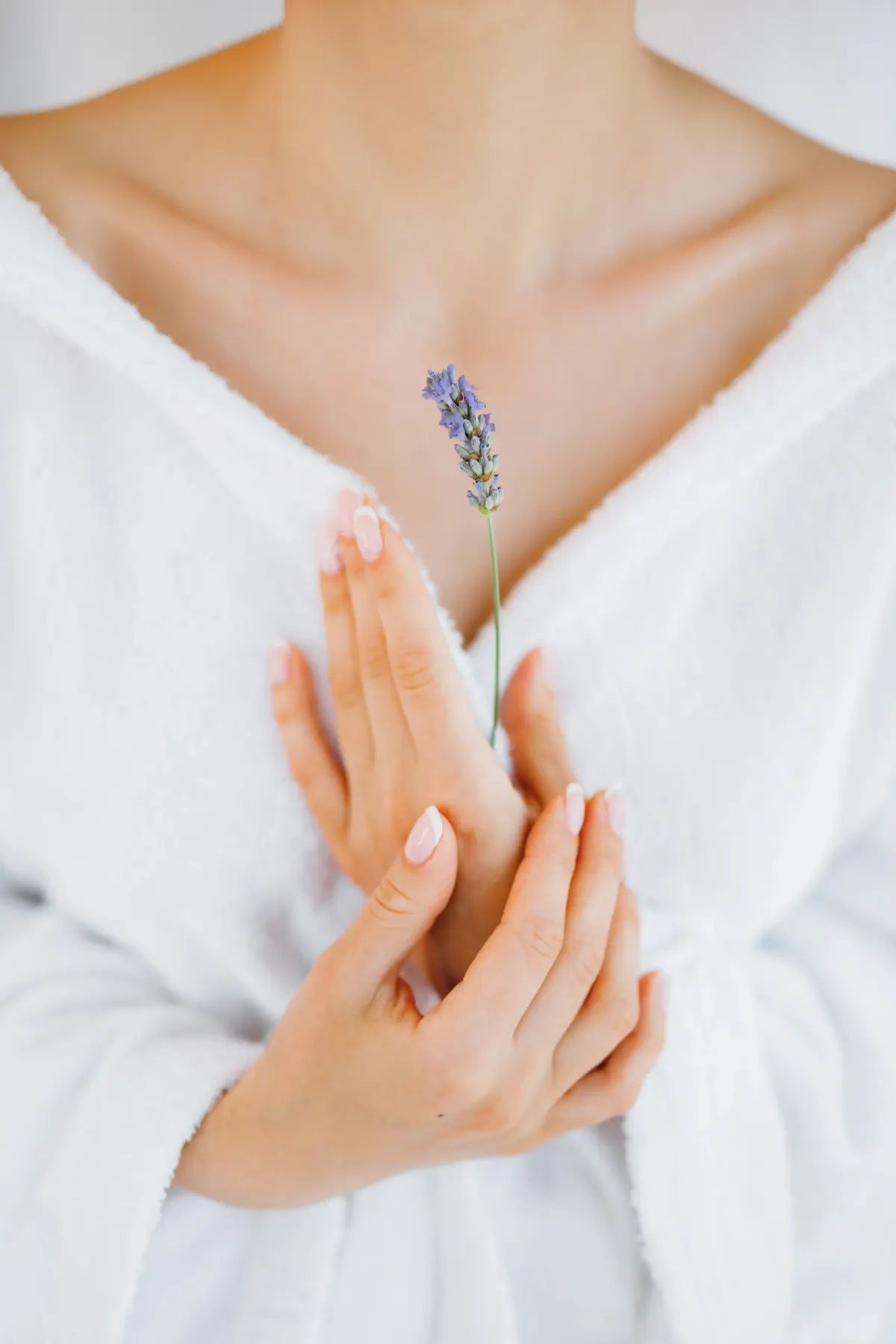 Woman in white robe holding lavender sprig against her chest, closeup