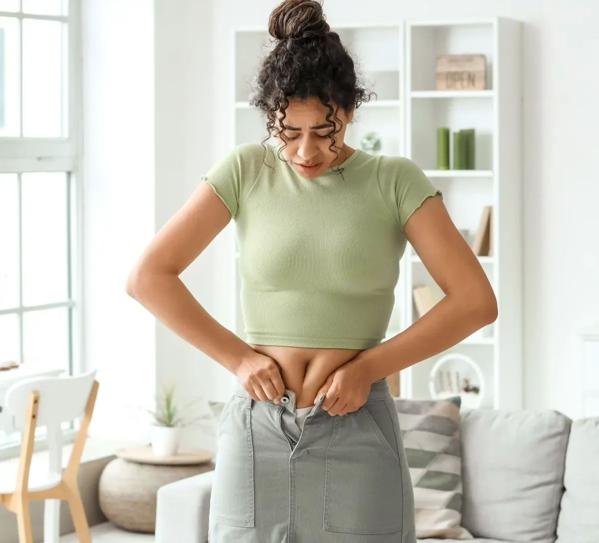 Woman in green top checking loose waistband of her pants at home