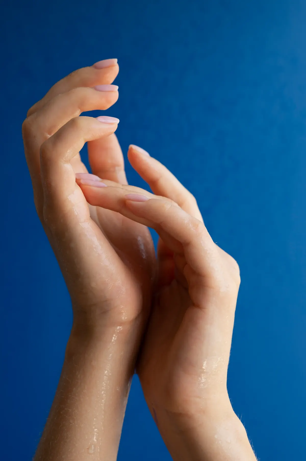 Woman's smooth youthful hands with manicured nails against blue background