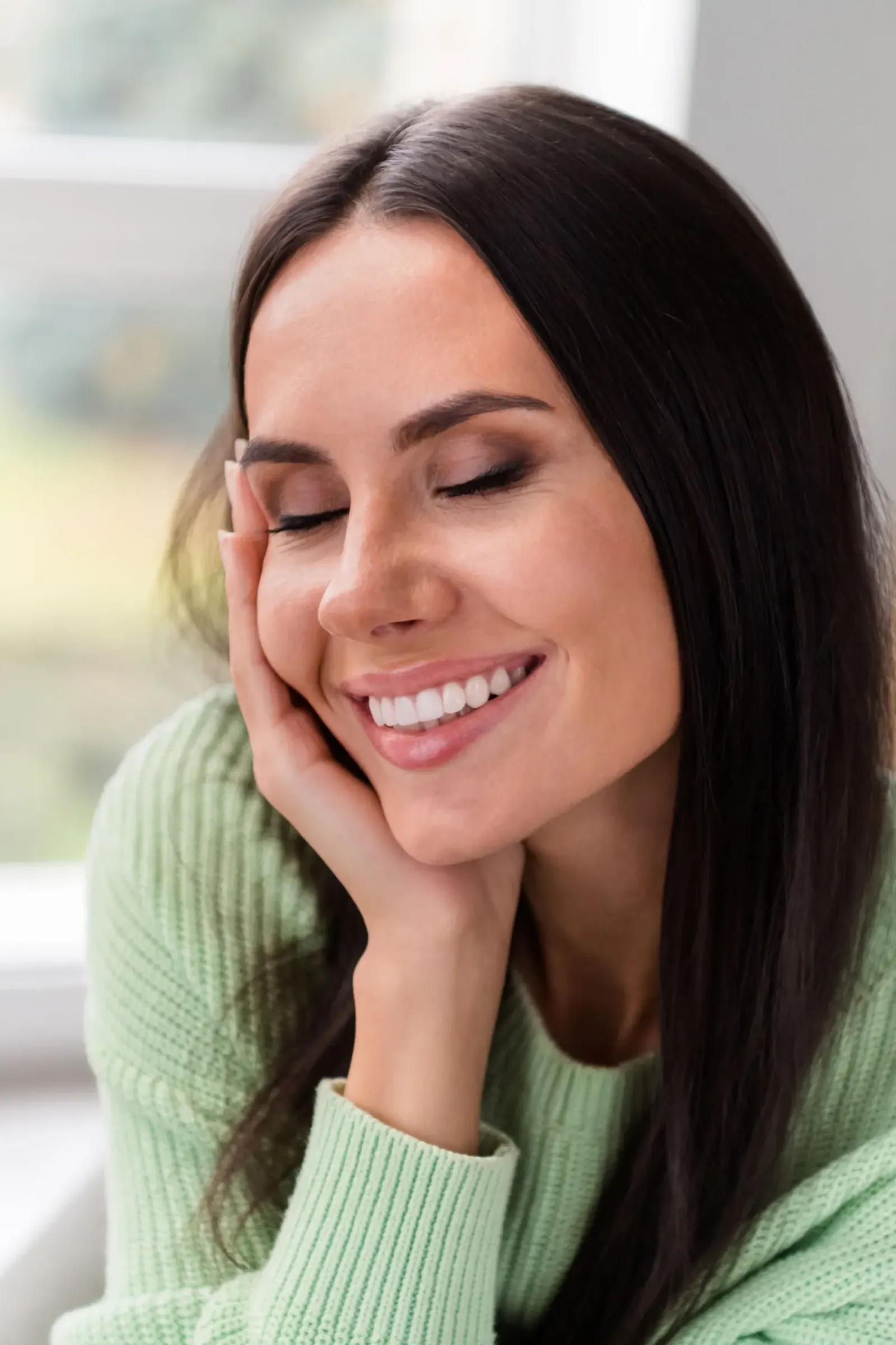 Smiling woman in green sweater resting her face on her hand with clear skin