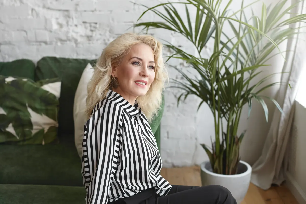 Smiling blonde woman relaxing on a couch beside a green plant