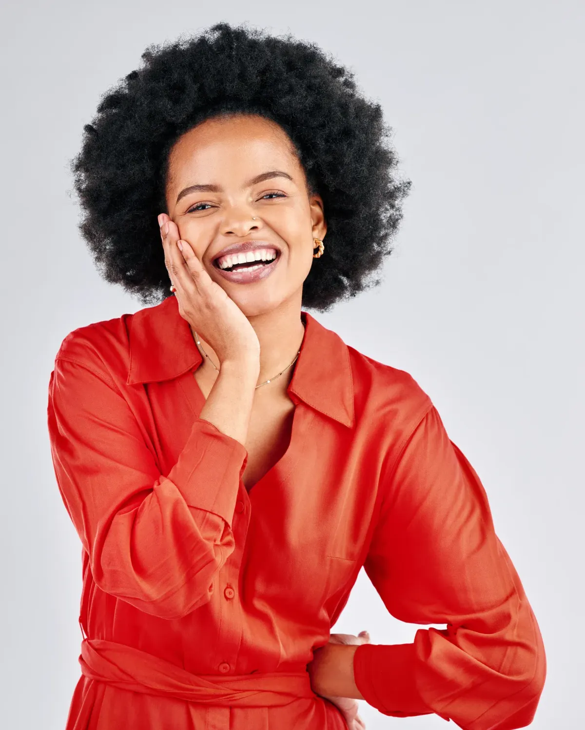 Smiling woman with afro hair in a red shirt touching her cheek