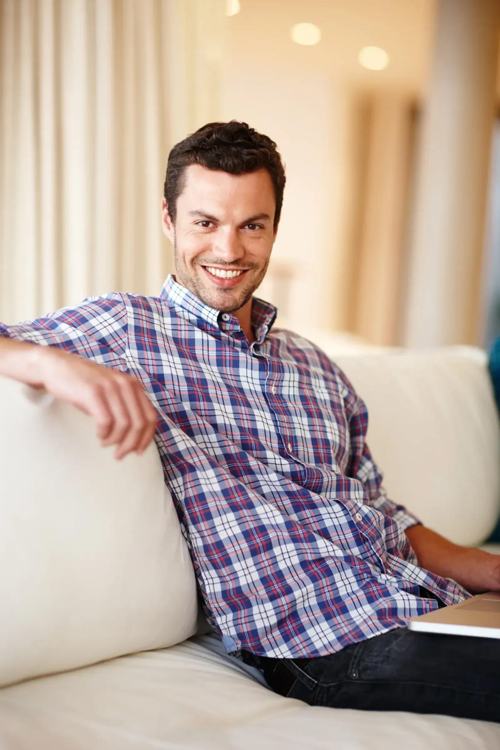Smiling man in plaid shirt relaxing on a couch at home