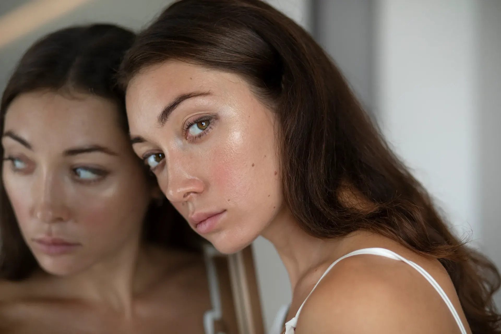 Young woman examining her dull, tired-looking complexion in a mirror
