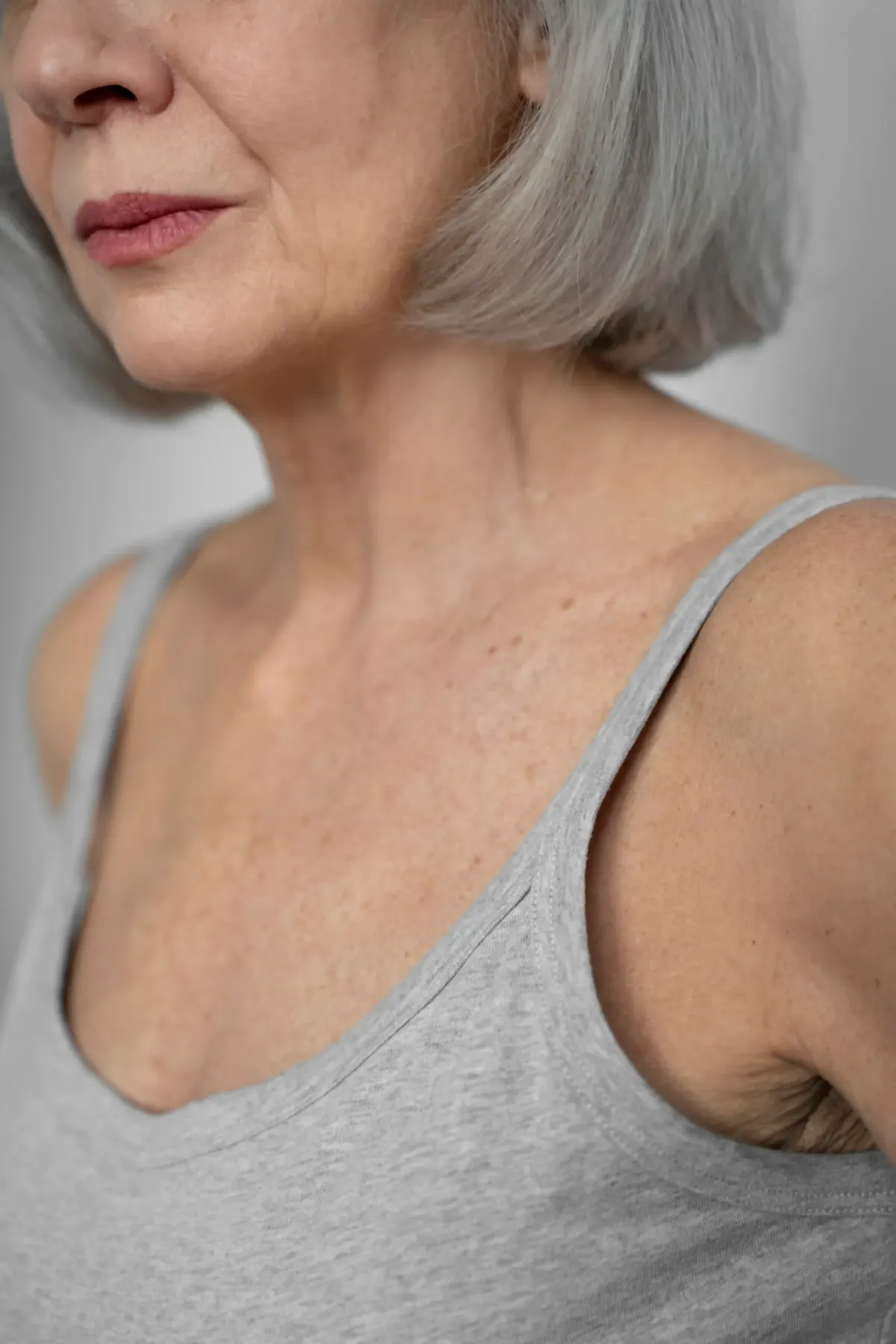 Older woman's neck and shoulder showing loose aging skin in gray tank top