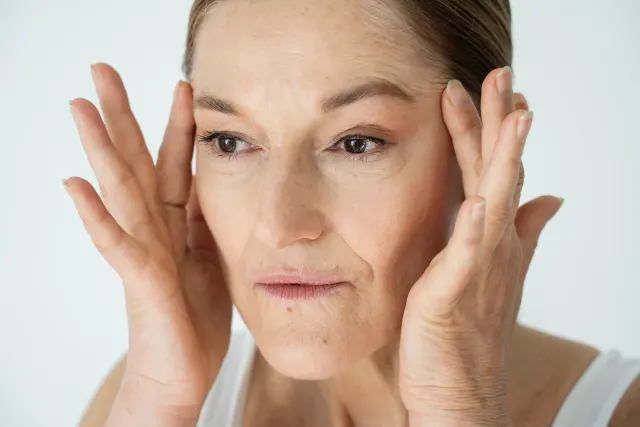 Mature woman gently lifting cheek skin with fingertips, showing facial lines