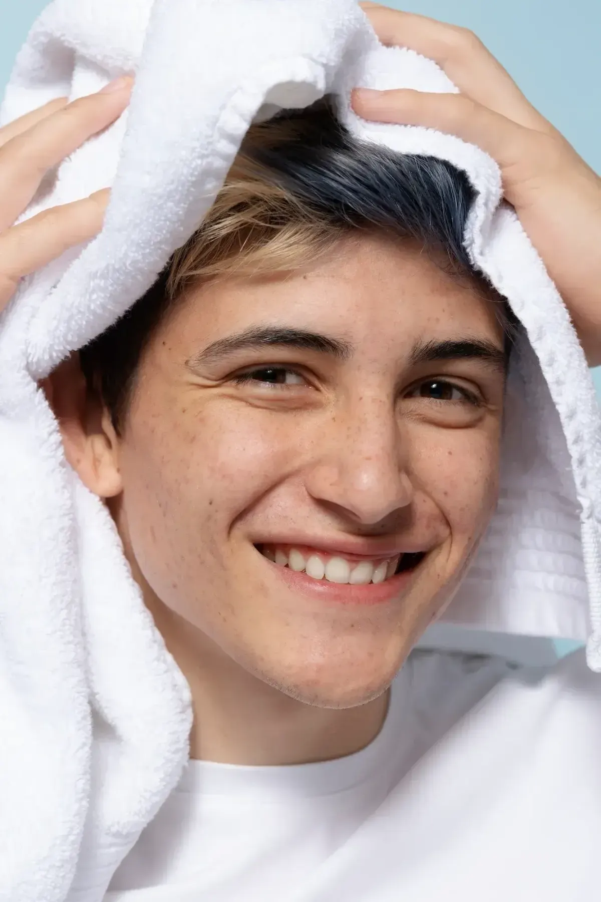 Smiling young man drying hair with white towel after washing