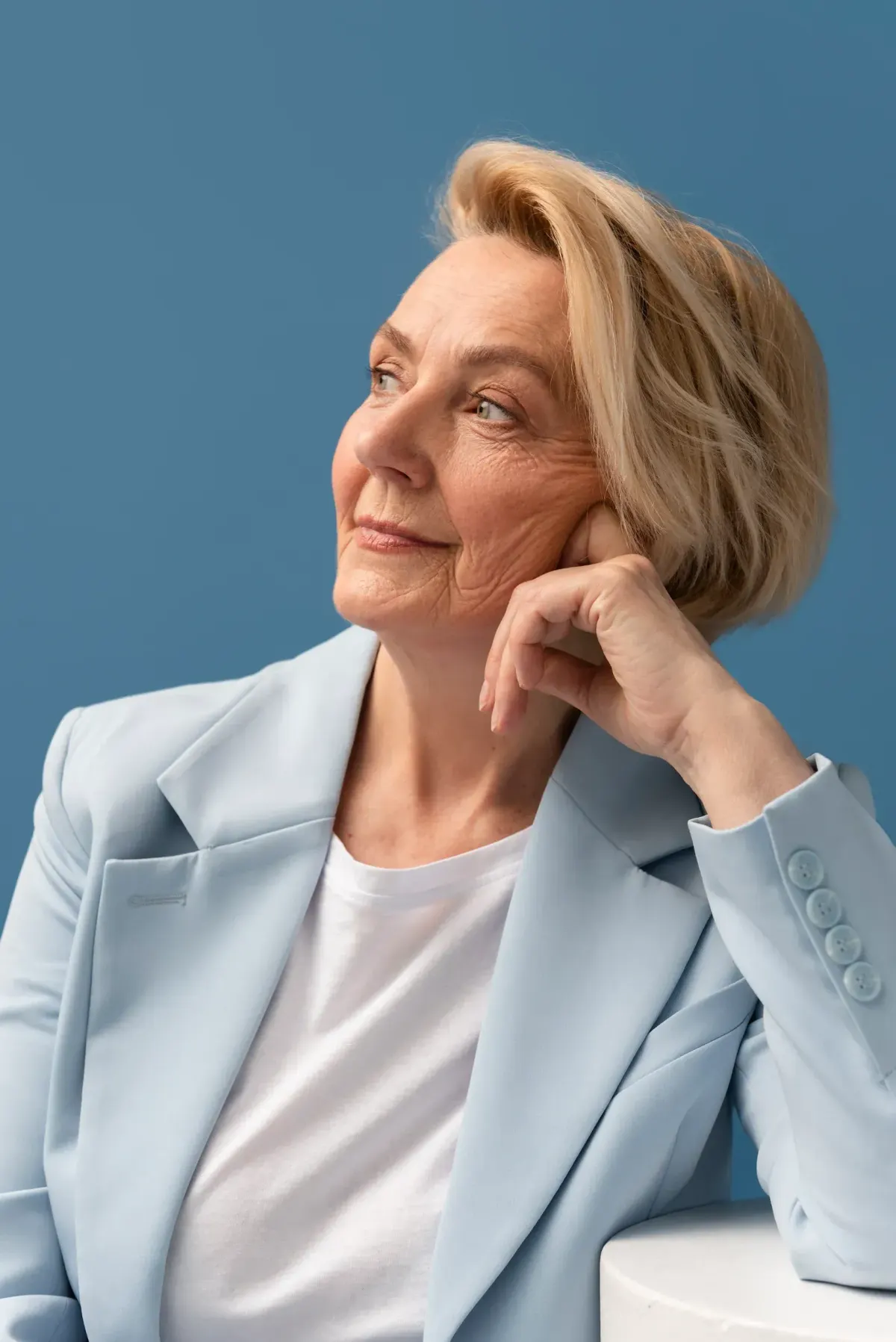 Smiling senior woman with short blonde hair in blue blazer resting on hand
