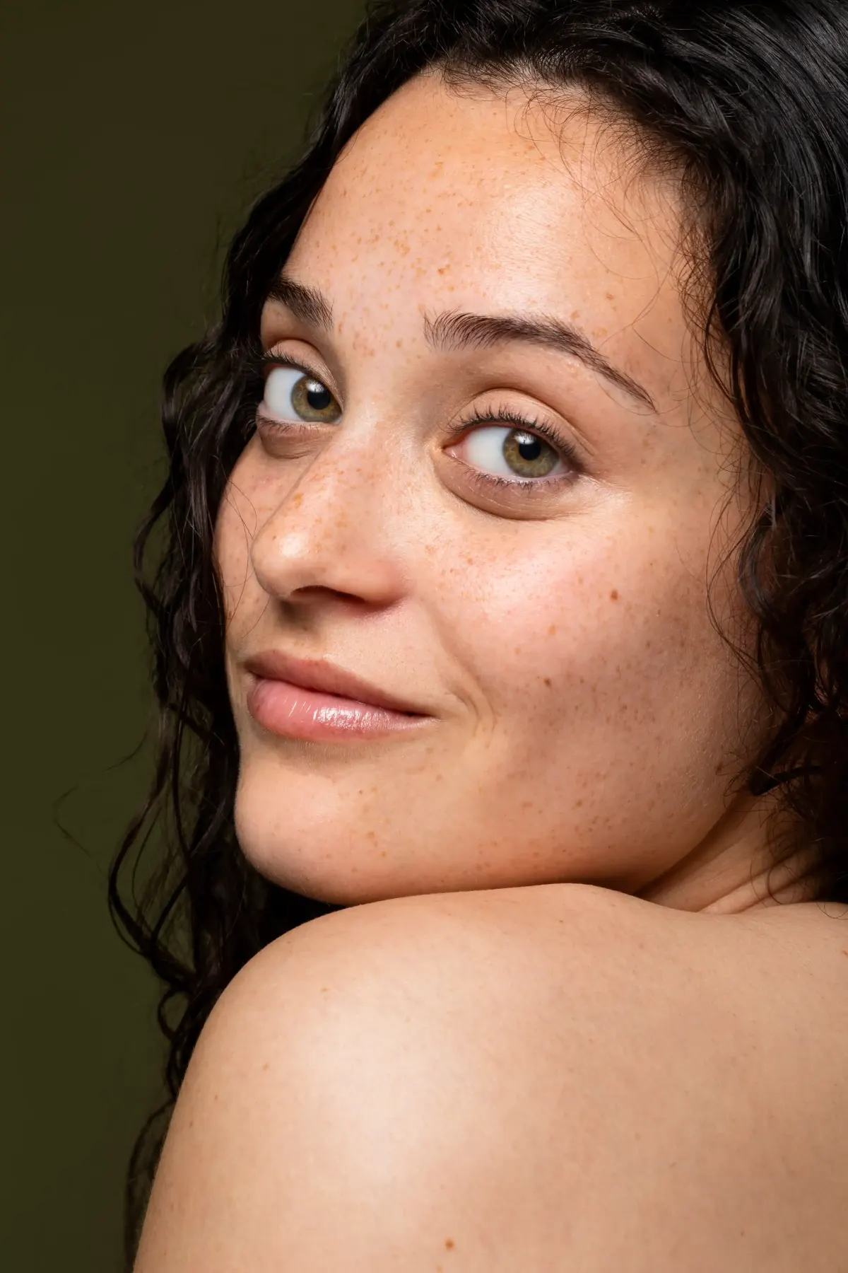 Smiling young woman with curly hair and healthy, glowing skin looking over her shoulder
