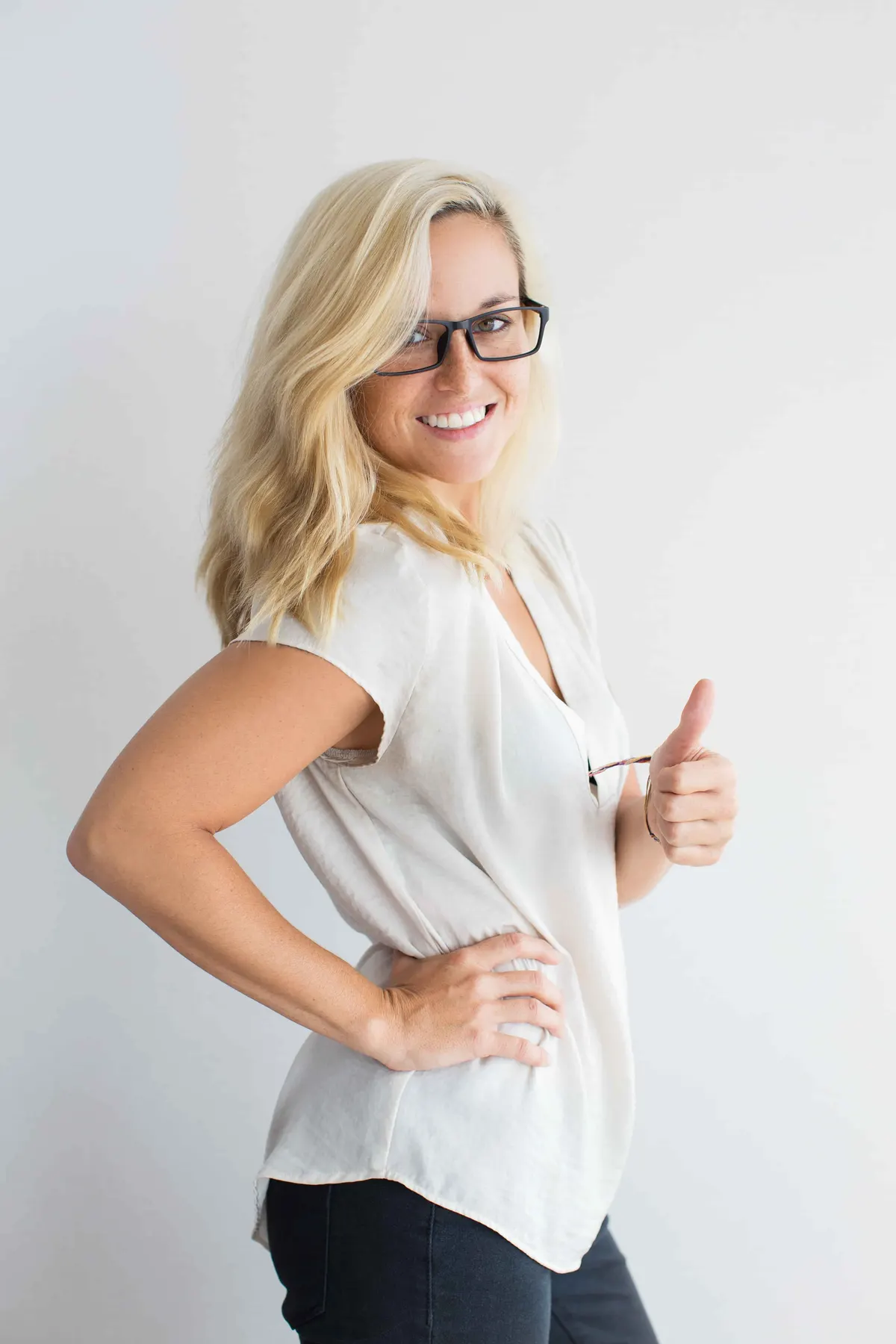 Smiling blonde woman in glasses and white blouse giving a thumbs up