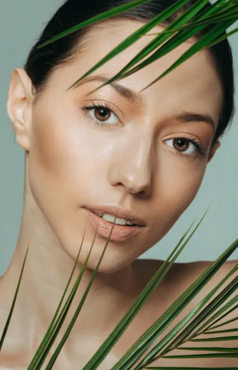 Woman with clear, glowing skin holding a palm leaf beside her face